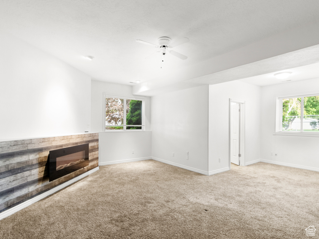 Unfurnished living room featuring light colored carpet, baseboards, a ceiling fan, and a glass covered fireplace