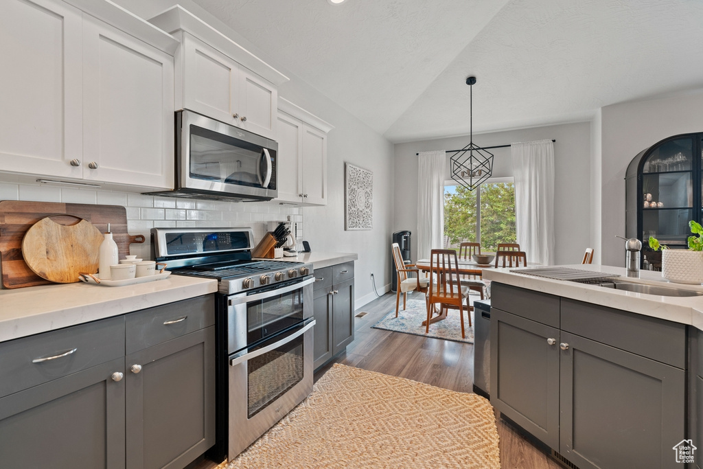 Kitchen with light countertops, wood finished floors, white cabinets, gray cabinetry, and appliances with stainless steel finishes