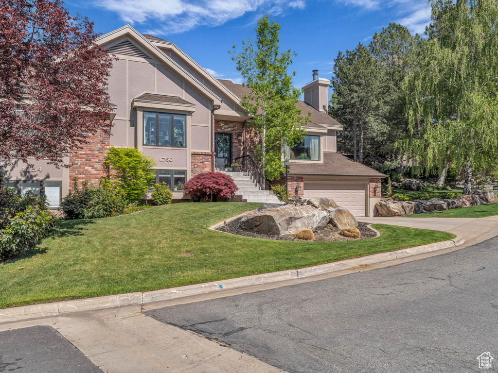 View of front of property with brick siding, a front lawn, an attached garage, and driveway