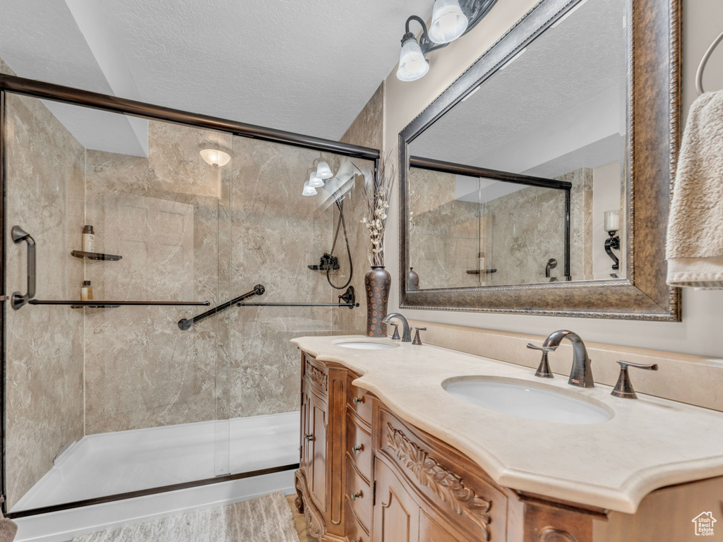 Bathroom featuring double vanity, a sink, a textured ceiling, and a stall shower