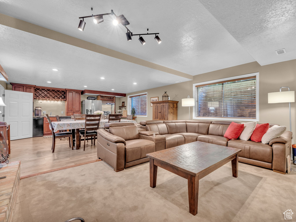 Living area featuring a textured ceiling, visible vents, light colored carpet, light wood-type flooring, and recessed lighting