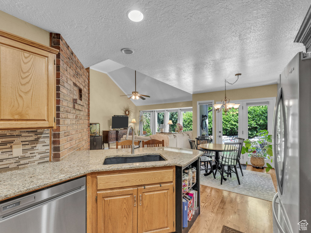 Kitchen featuring a peninsula, a textured ceiling, a sink, light wood finished floors, and stainless steel appliances