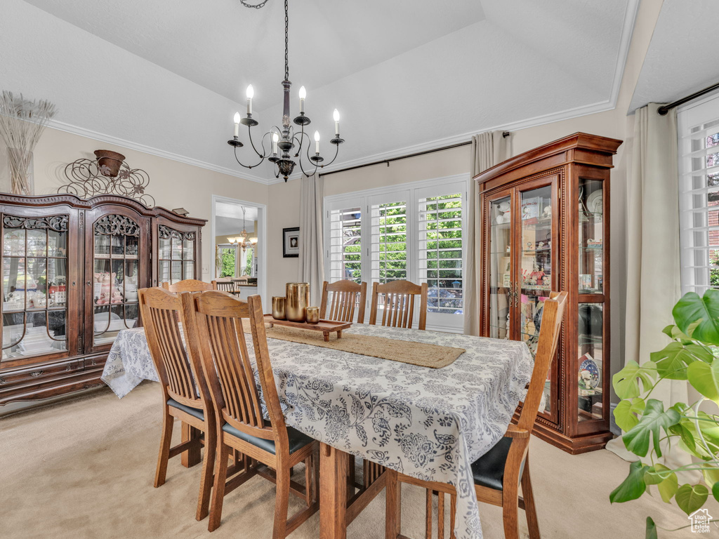 Dining space with an inviting chandelier, ornamental molding, vaulted ceiling, and light colored carpet