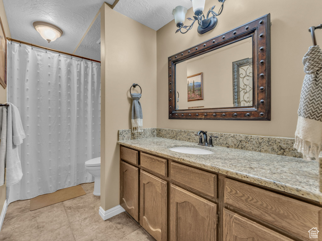Full bath featuring vanity, tile patterned flooring, toilet, a textured ceiling, and a notable chandelier