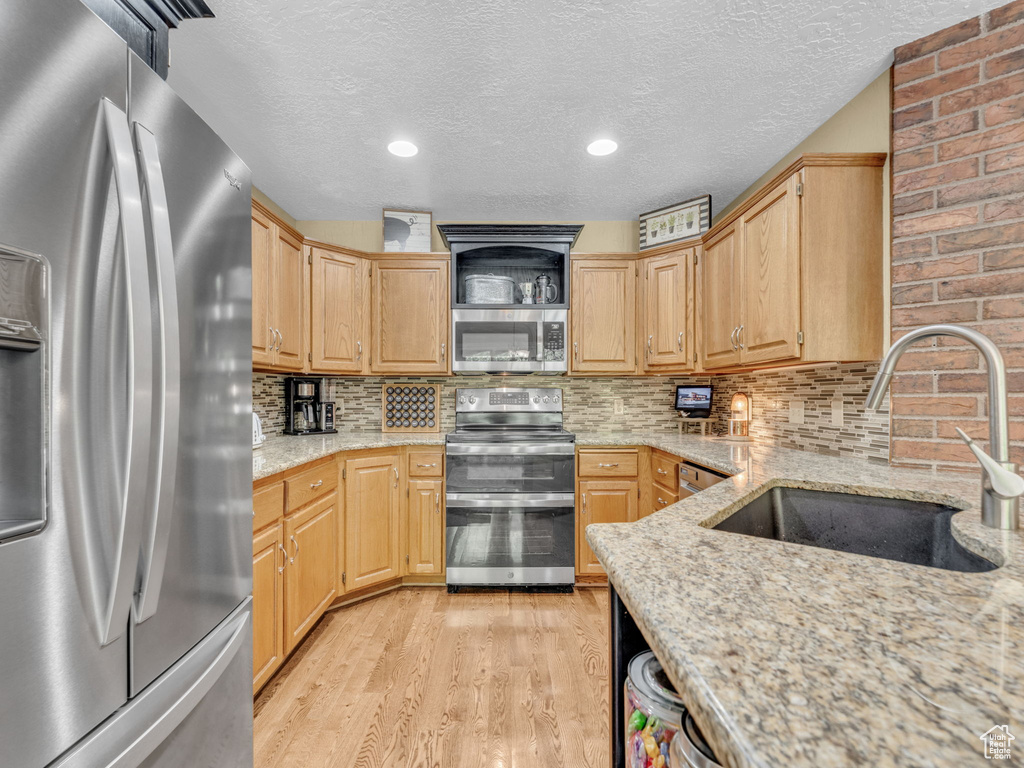 Kitchen with light wood-type flooring, a textured ceiling, a sink, backsplash, and stainless steel appliances