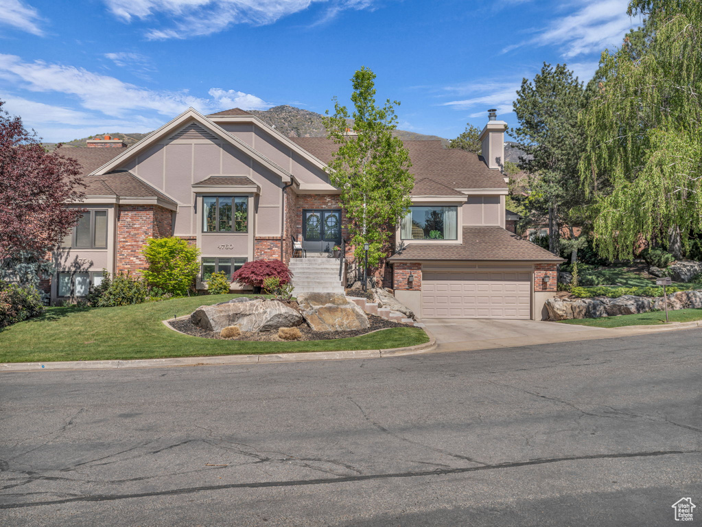 Craftsman-style house featuring a front lawn, a chimney, brick siding, concrete driveway, and an attached garage
