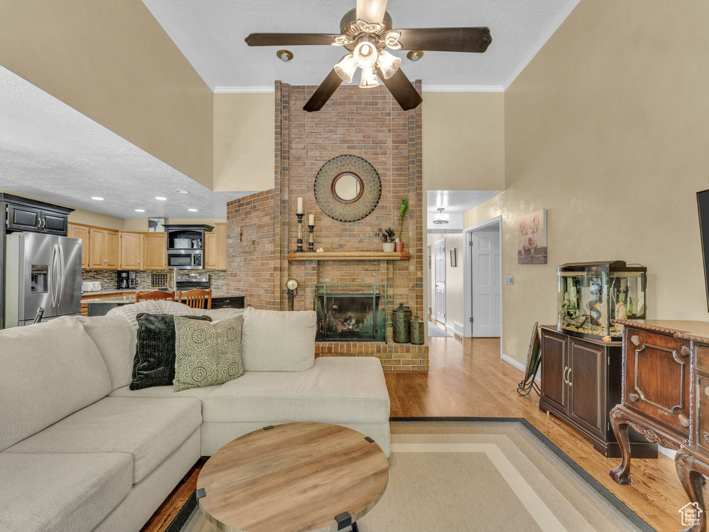 Living area with a brick fireplace, a ceiling fan, light wood finished floors, and a towering ceiling