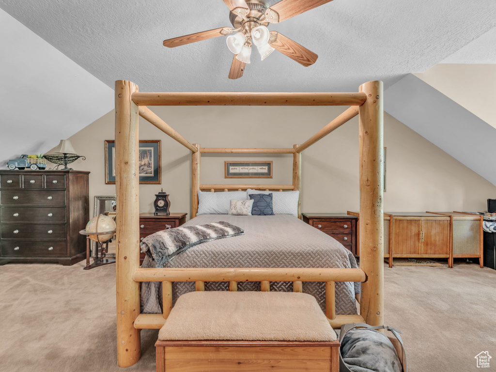 Carpeted bedroom with ceiling fan, vaulted ceiling, and a textured ceiling