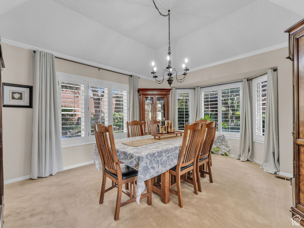 Dining space featuring an inviting chandelier, crown molding, lofted ceiling, baseboards, and light colored carpet