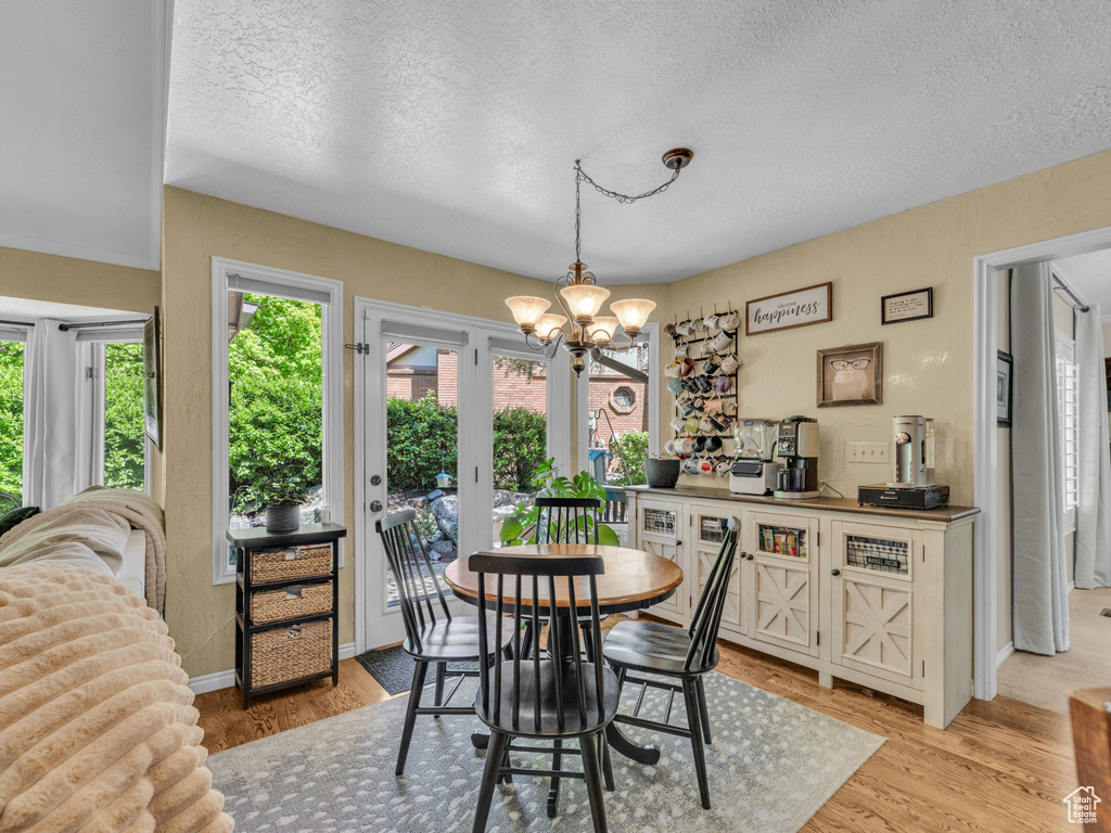 Dining area featuring baseboards, a textured ceiling, an inviting chandelier, and light wood-style flooring