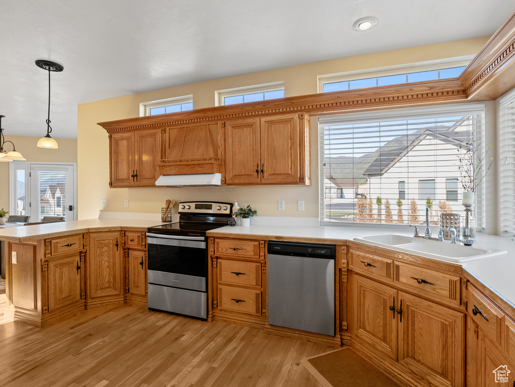 Kitchen featuring a peninsula, a sink, stainless steel appliances, under cabinet range hood, and light wood-style floors