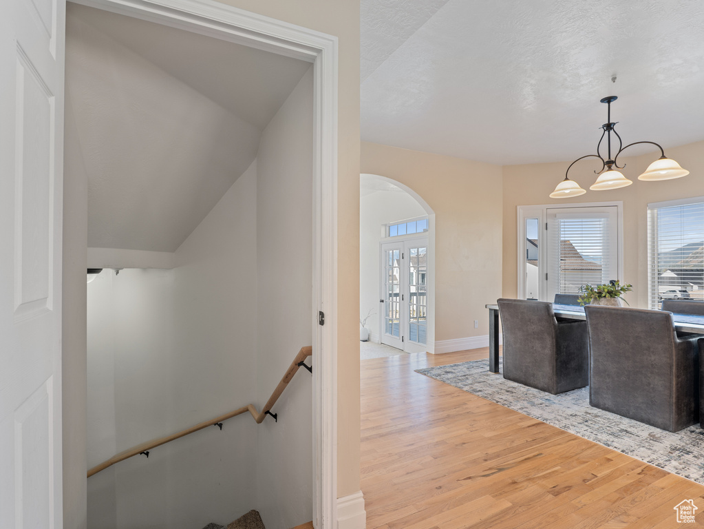 Interior space with an inviting chandelier, an upstairs landing, baseboards, arched walkways, and light wood-style floors