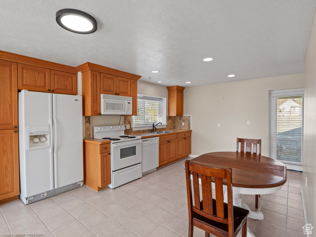 Kitchen with backsplash, brown cabinetry, a sink, and white appliances