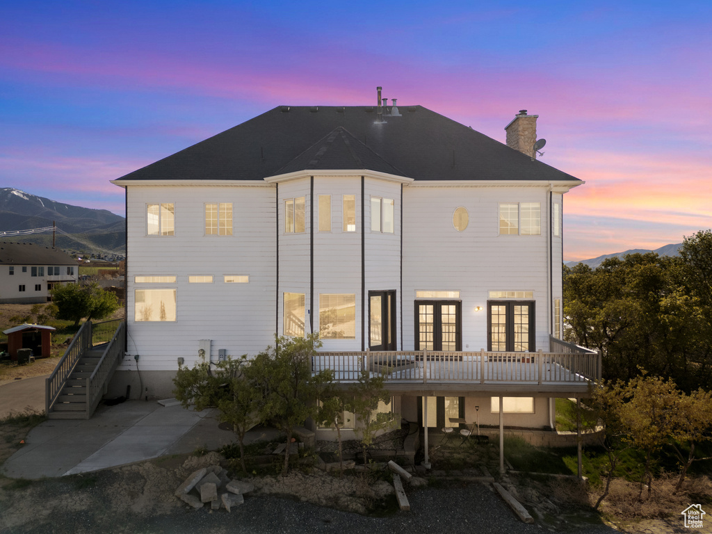 Rear view of house featuring a deck, french doors, a patio, stairway, and a chimney