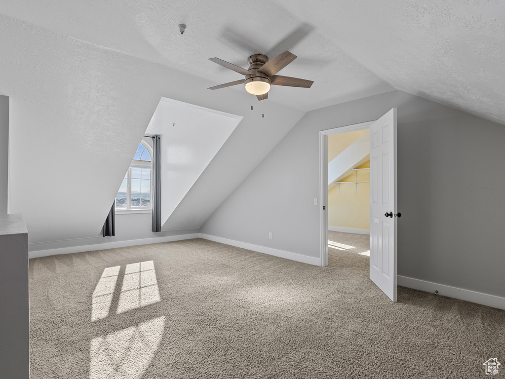 Additional living space with carpet floors, a textured ceiling, baseboards, ceiling fan, and vaulted ceiling