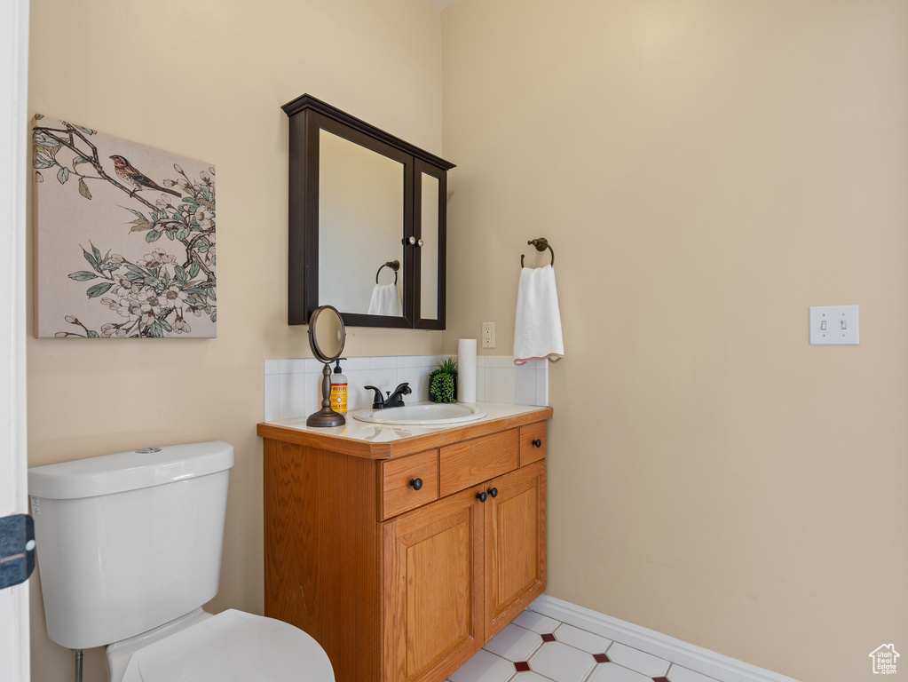Half bathroom with toilet, baseboards, tile patterned floors, and vanity