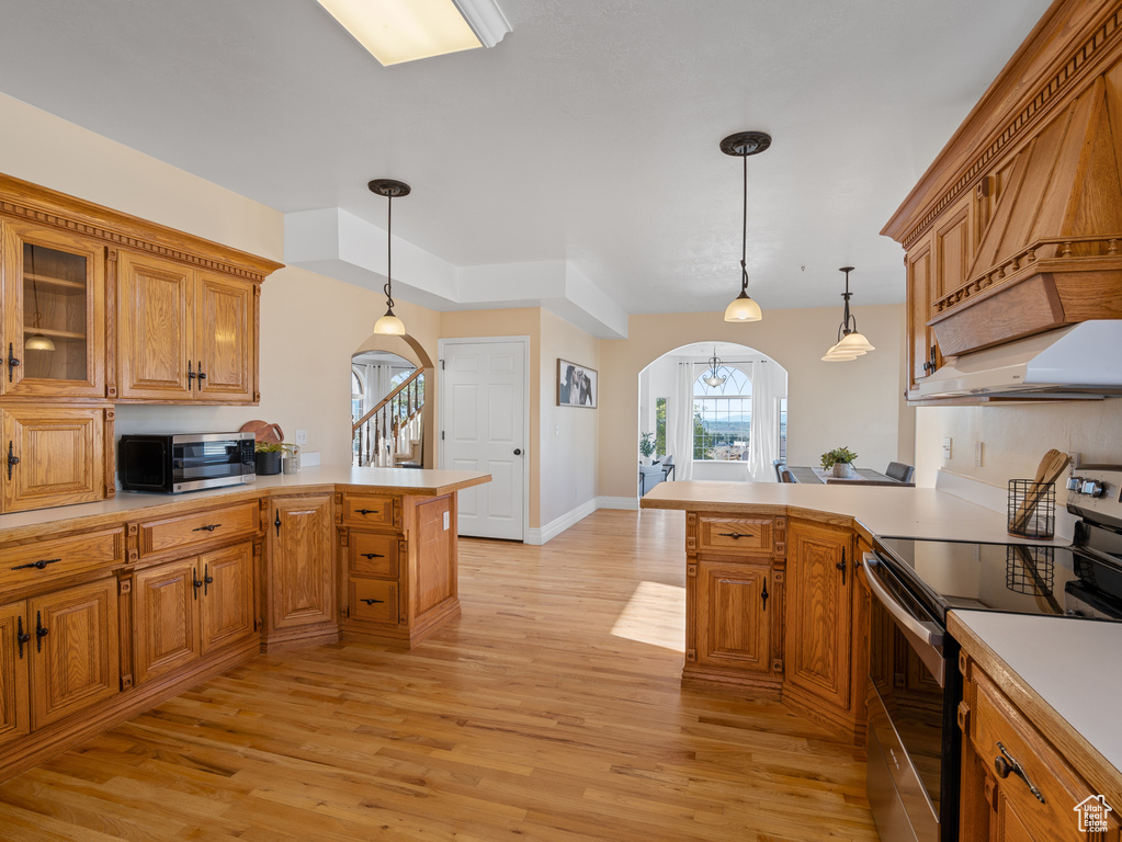 Kitchen featuring light wood-style flooring, a peninsula, arched walkways, light countertops, and appliances with stainless steel finishes