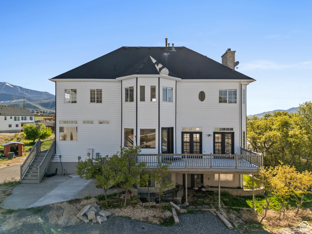 Rear view of property featuring a chimney, french doors, a deck with mountain view, a patio, and stairs