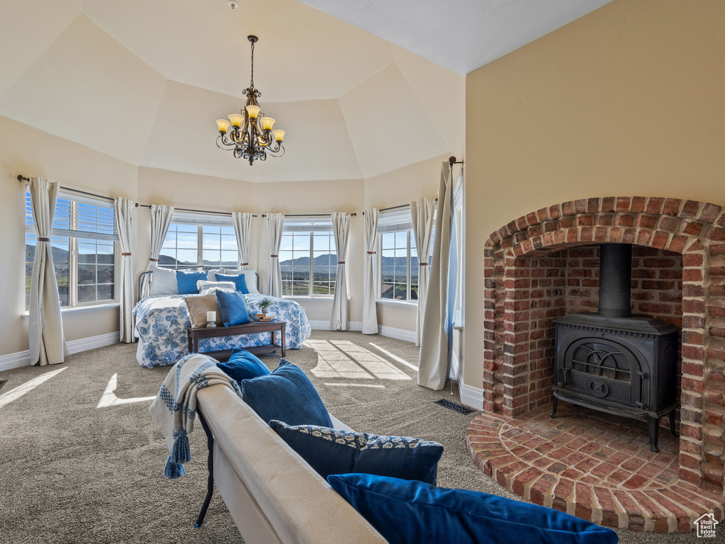 Carpeted bedroom with an inviting chandelier, high vaulted ceiling, visible vents, baseboards, and a wood stove
