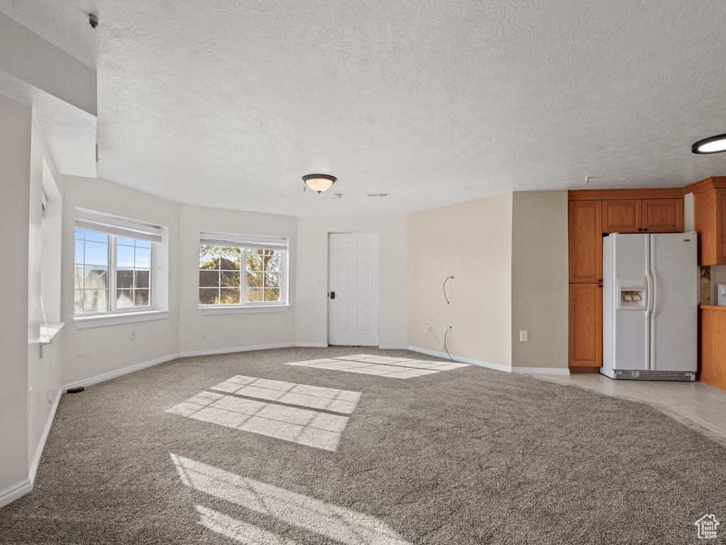 Unfurnished living room with light carpet, a textured ceiling, and baseboards