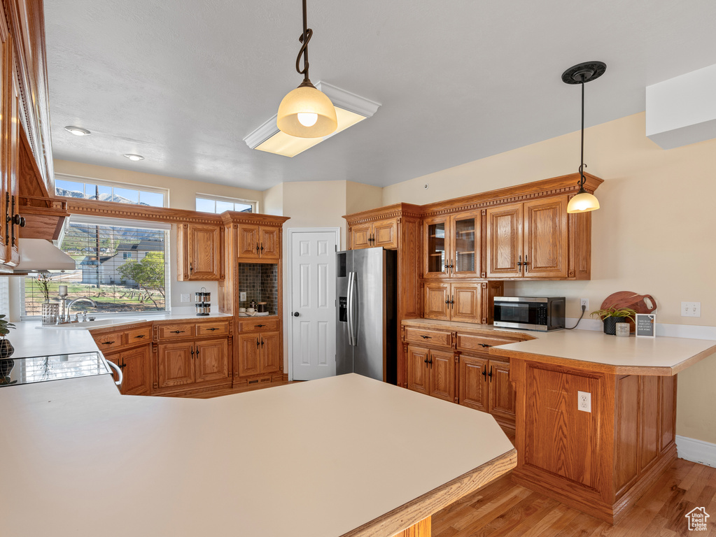 Kitchen with light wood-type flooring, light countertops, a peninsula, and appliances with stainless steel finishes