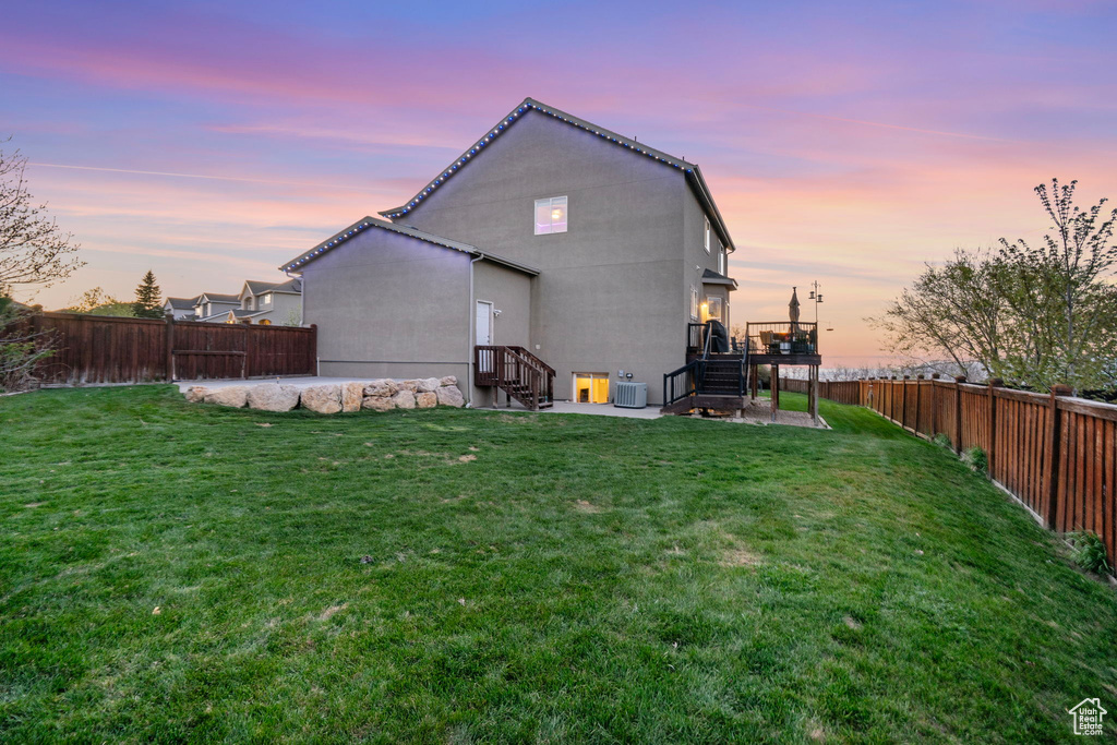 Back of property at dusk featuring stairway, a wooden deck, a lawn, and a fenced backyard