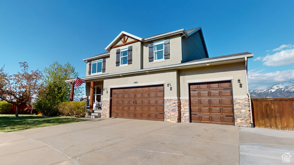 View of front of house with an attached garage, stucco siding, stone siding, and fence