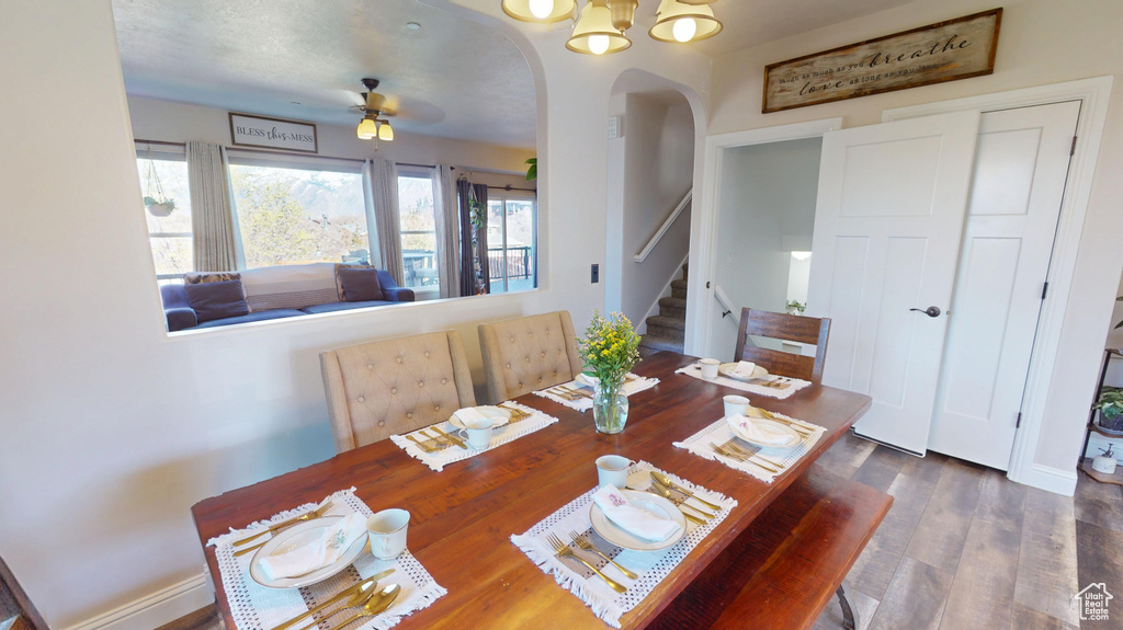 Dining room with arched walkways, ceiling fan with notable chandelier, wood finished floors, and stairway