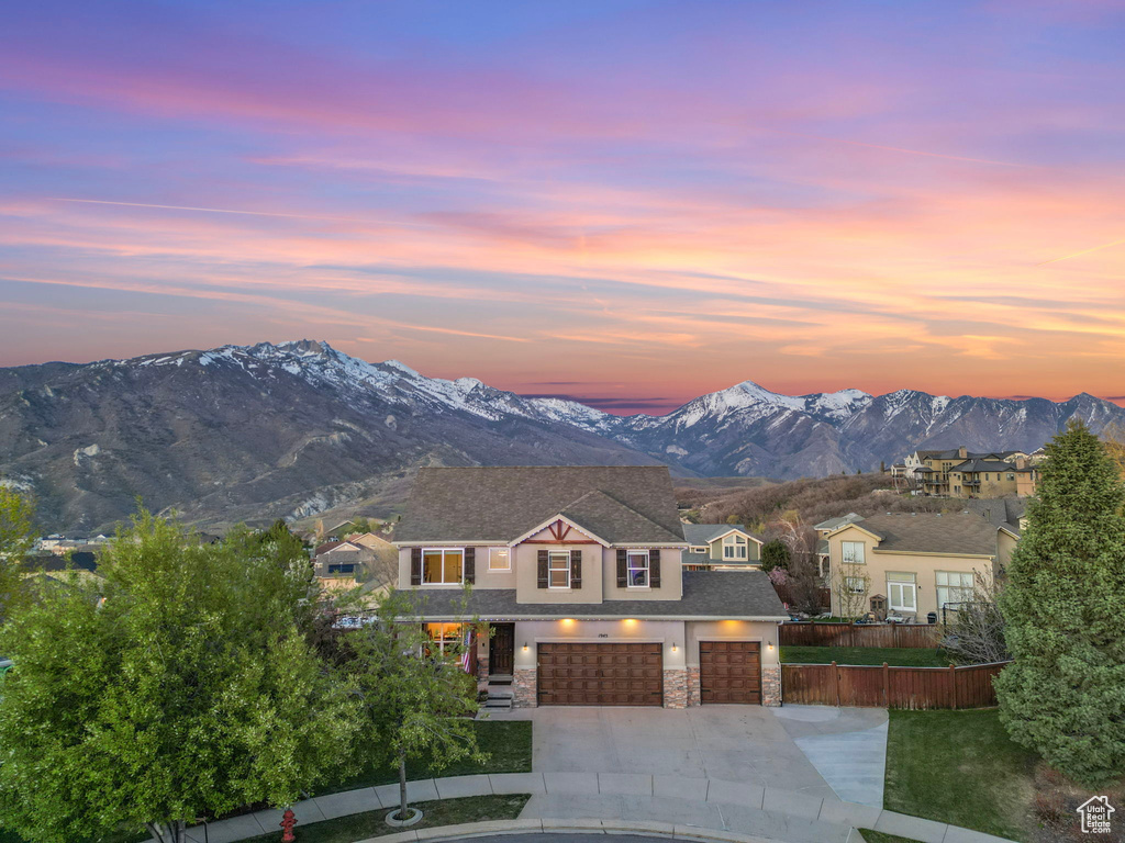 View of front of property with fence, a mountain view, stone siding, concrete driveway, and a garage