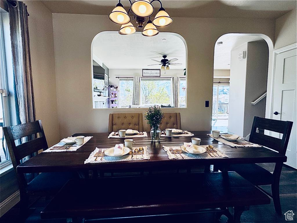 Dining space featuring arched walkways, a healthy amount of sunlight, and ceiling fan with notable chandelier