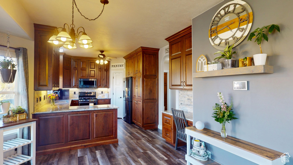 Kitchen with backsplash, dark wood-style flooring, appliances with stainless steel finishes, and ceiling fan with notable chandelier