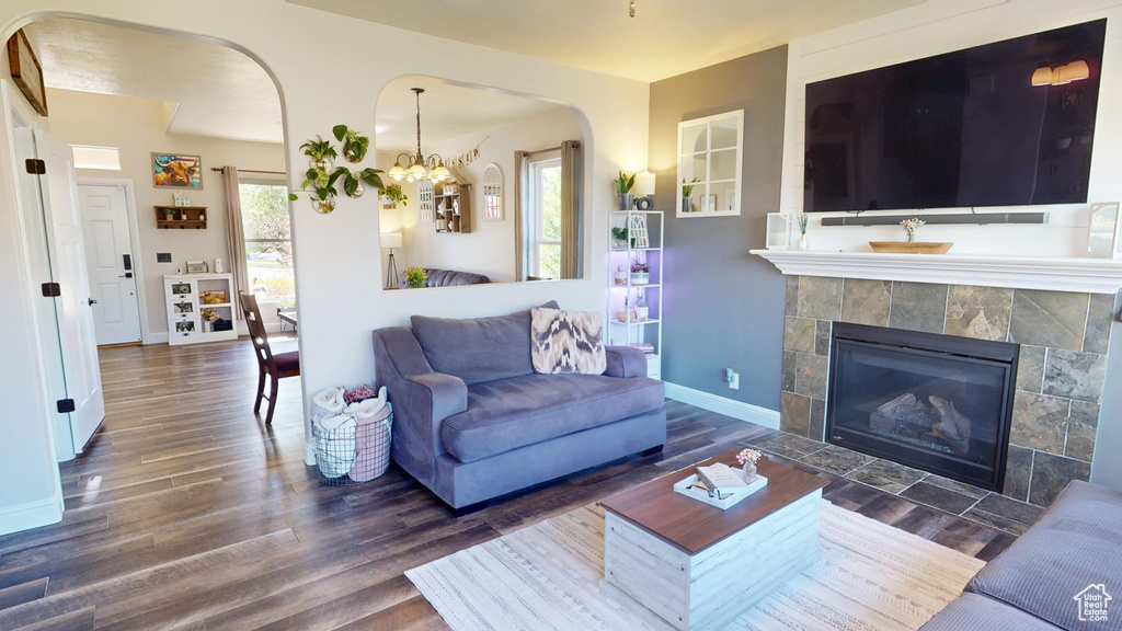 Living room with a tiled fireplace, arched walkways, baseboards, and wood finished floors