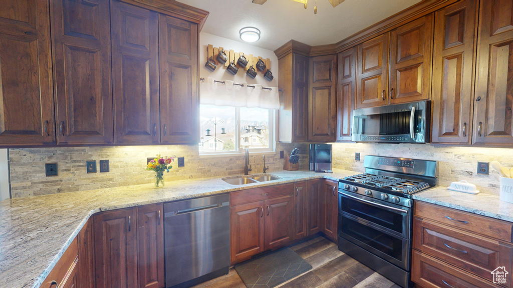 Kitchen featuring appliances with stainless steel finishes, light stone counters, a sink, decorative backsplash, and dark wood-type flooring