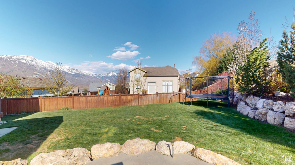 View of yard with a trampoline, a mountain view, and fence