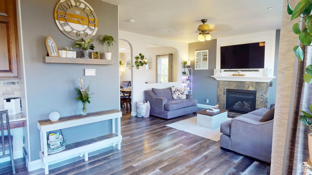 Living area with arched walkways, ceiling fan, a fireplace, and wood finished floors