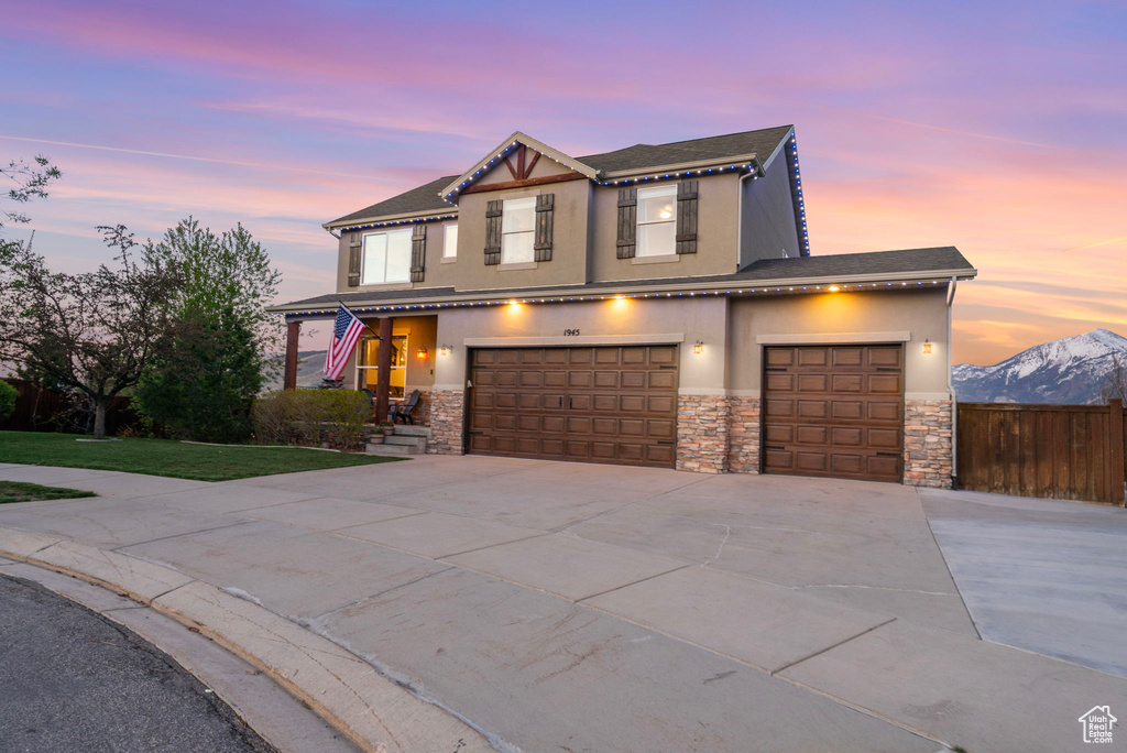View of front of property with concrete driveway, stone siding, stucco siding, and fence
