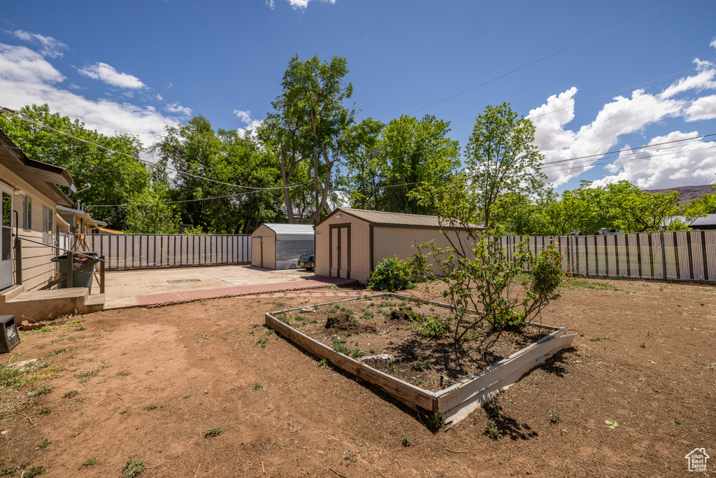 Fenced backyard with a storage unit, an outbuilding, and a vegetable garden