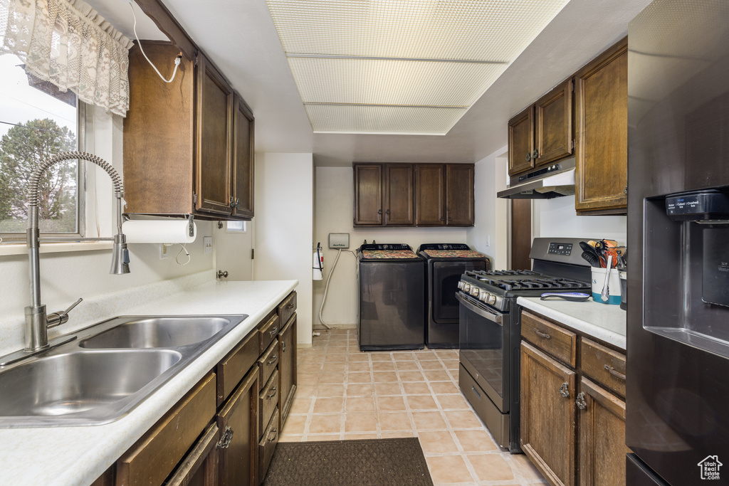 Kitchen featuring appliances with stainless steel finishes, washer and dryer, a sink, under cabinet range hood, and light countertops