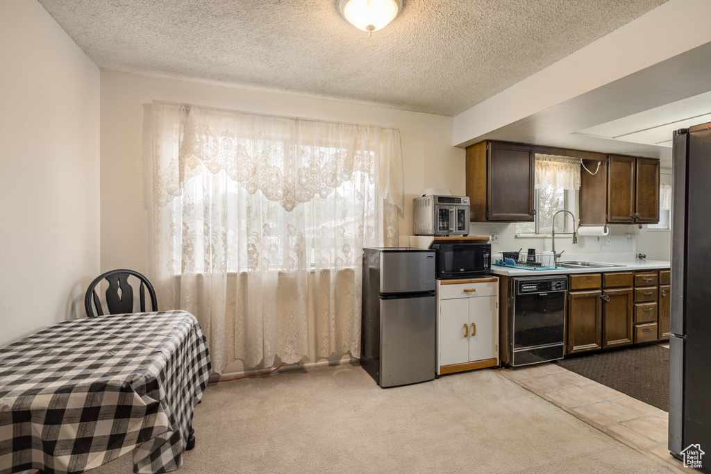 Kitchen featuring black appliances, a sink, light colored carpet, a textured ceiling, and light countertops