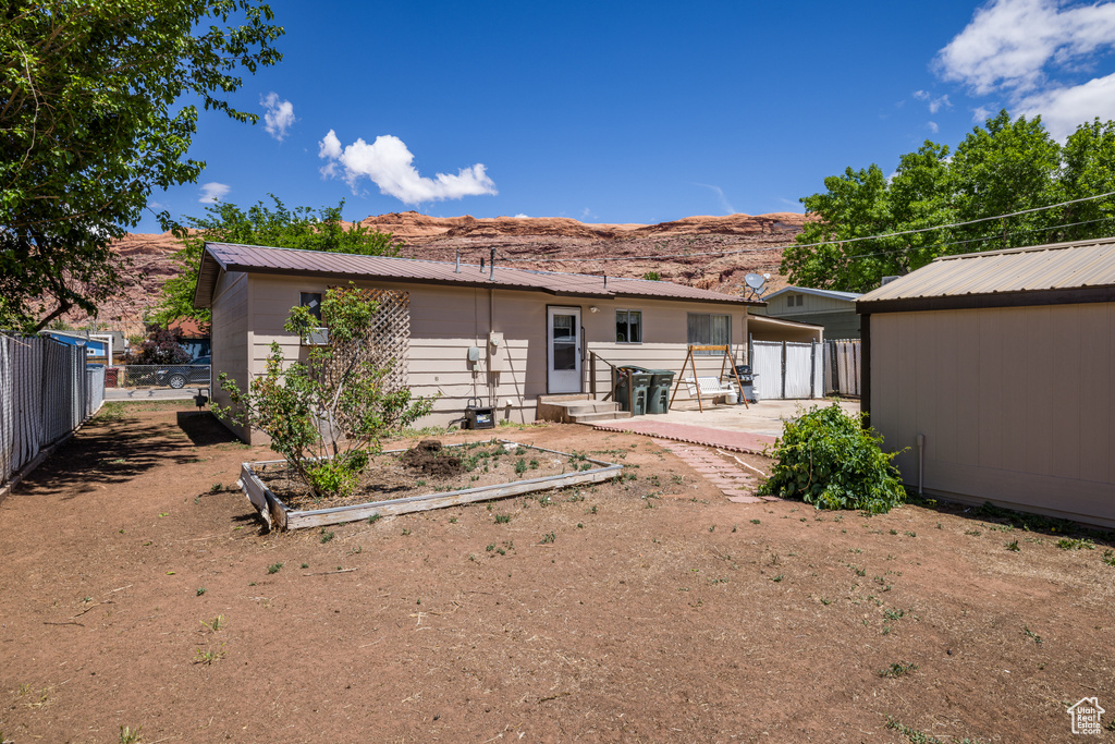 Rear view of house featuring fence, metal roof, a patio, a mountain view, and a vegetable garden
