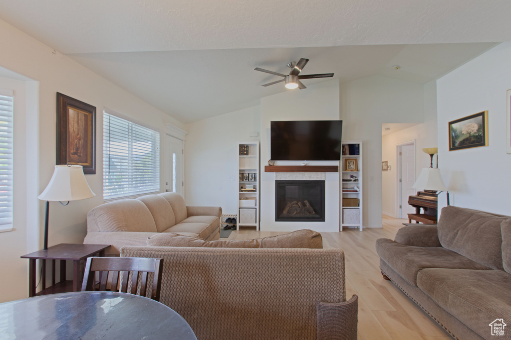 Living area with a ceiling fan, a glass covered fireplace, light wood-type flooring, and high vaulted ceiling