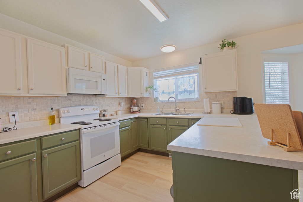 Kitchen featuring white appliances, a sink, a peninsula, green cabinetry, and tasteful backsplash