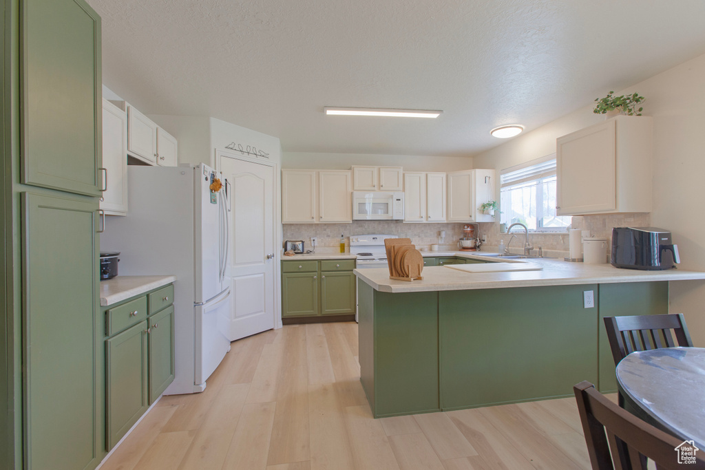 Kitchen with green cabinets, white appliances, a sink, a peninsula, and light wood-style floors