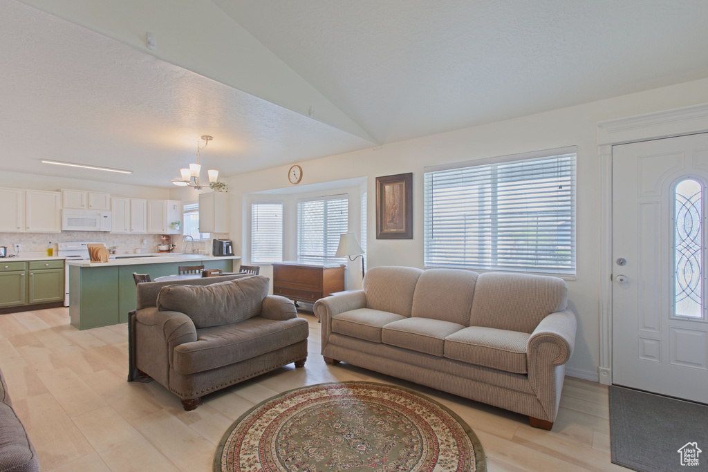 Living room with an inviting chandelier, light wood-style floors, and lofted ceiling