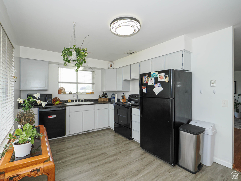 Kitchen with black appliances, a sink, dark countertops, and light wood-type flooring