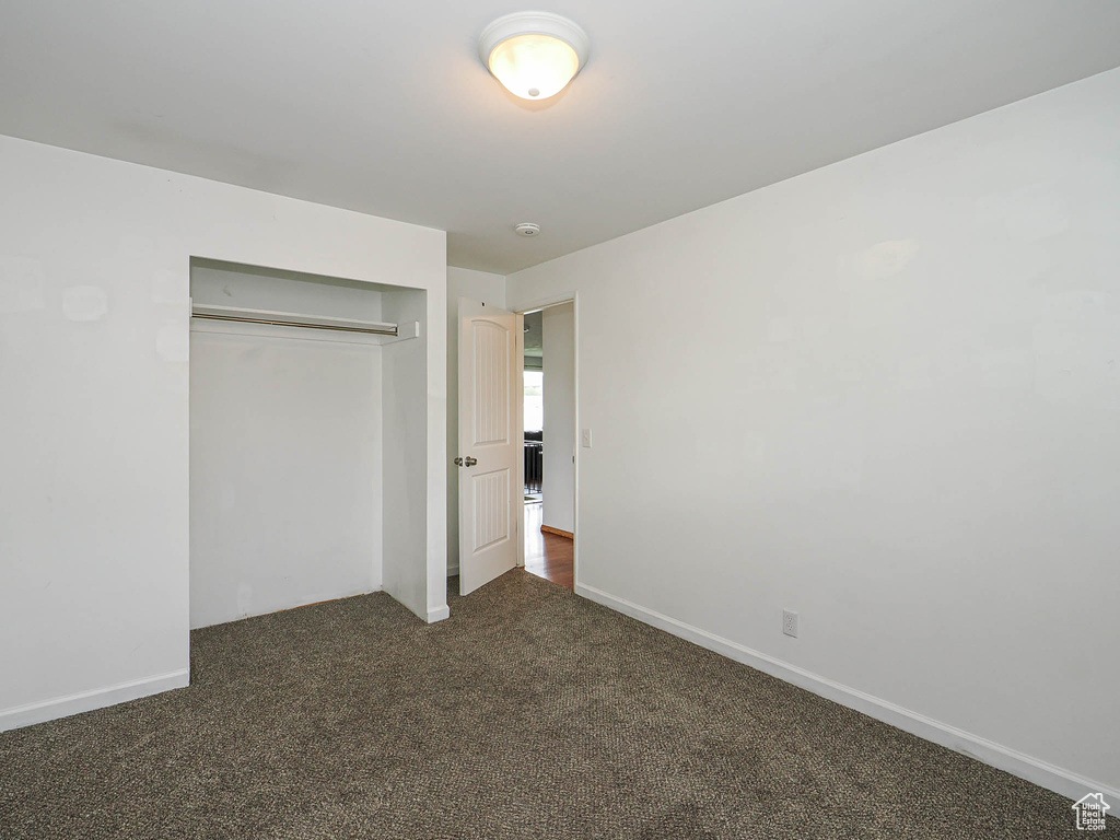 Unfurnished bedroom with dark colored carpet, a closet, and baseboards