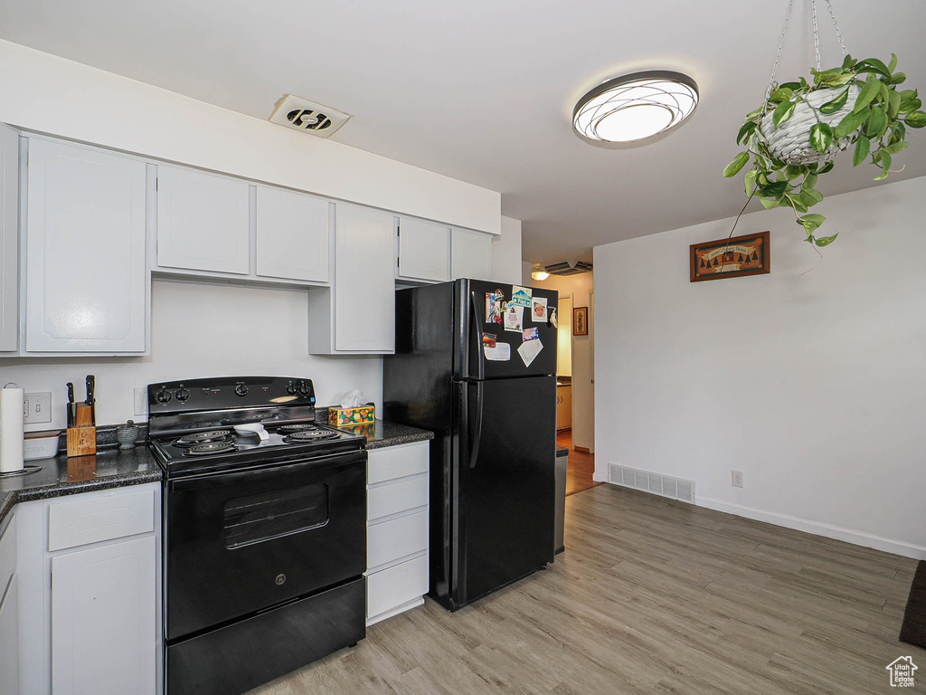 Kitchen featuring black appliances, light wood finished floors, dark stone countertops, white cabinets, and baseboards