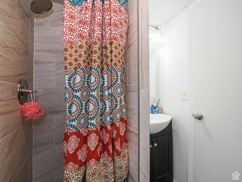 Bathroom with tiled shower, vanity, and a textured ceiling