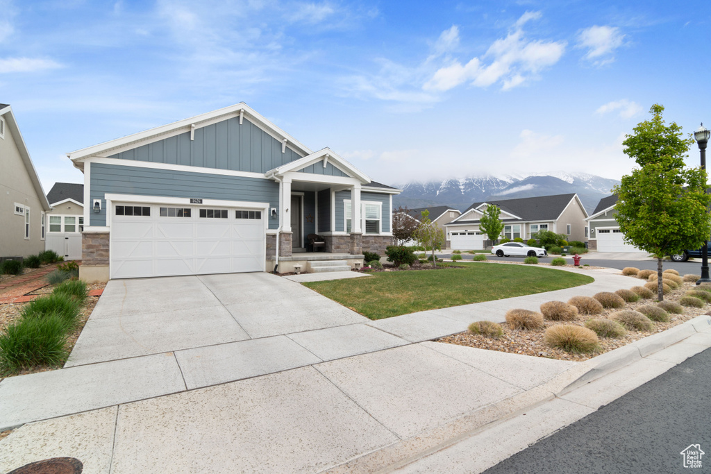 Craftsman-style house with board and batten siding, an attached garage, concrete driveway, a front lawn, and a mountain view