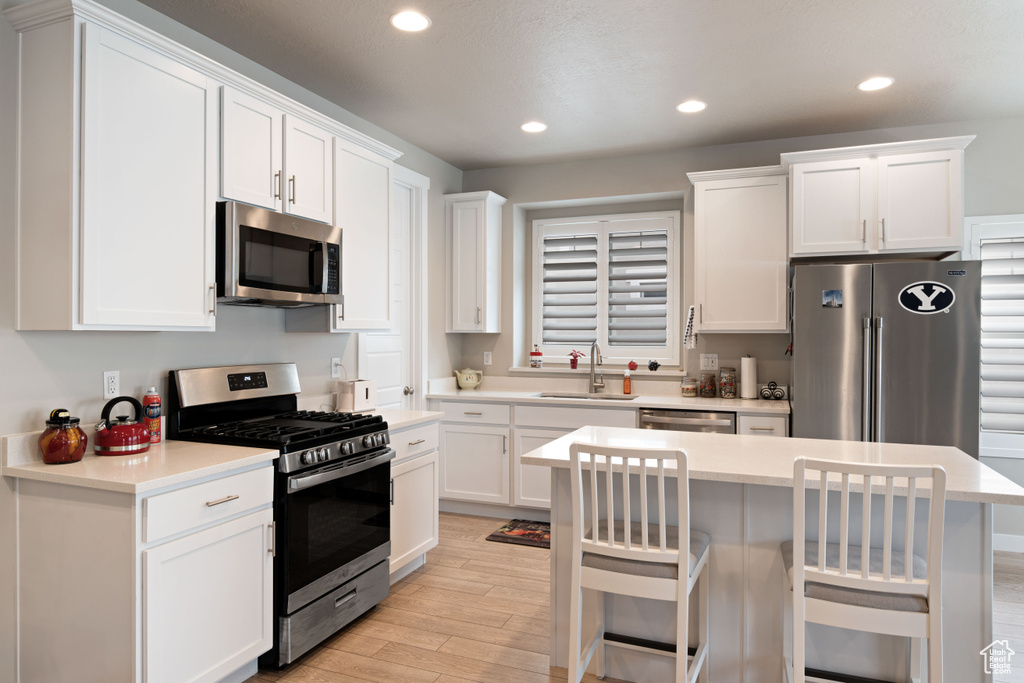 Kitchen with appliances with stainless steel finishes, a sink, white cabinetry, light wood-type flooring, and recessed lighting